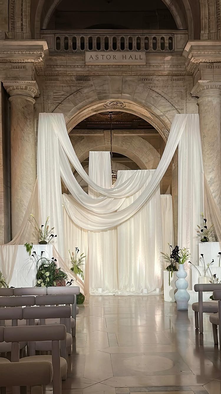 Wedding ceremony setup in Astor Hall with white fabric drapes and stone architecture.