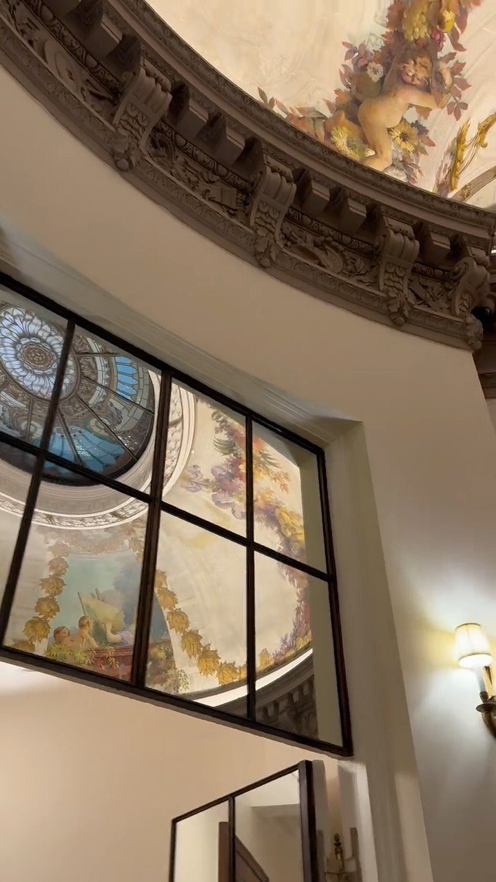 Ornate interior architecture with a painted ceiling and reflective glass windows.