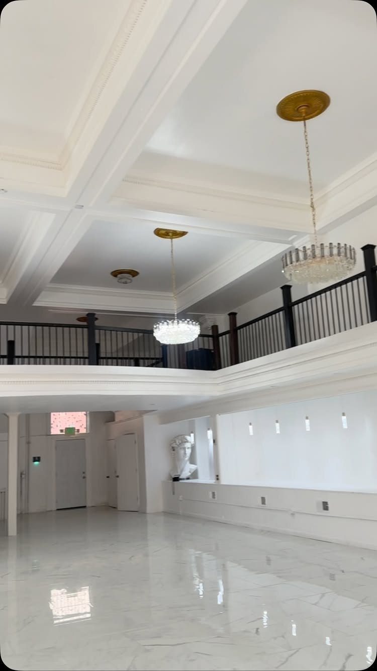 Empty white event space with marble floors, crystal chandeliers, and a mezzanine balcony.
