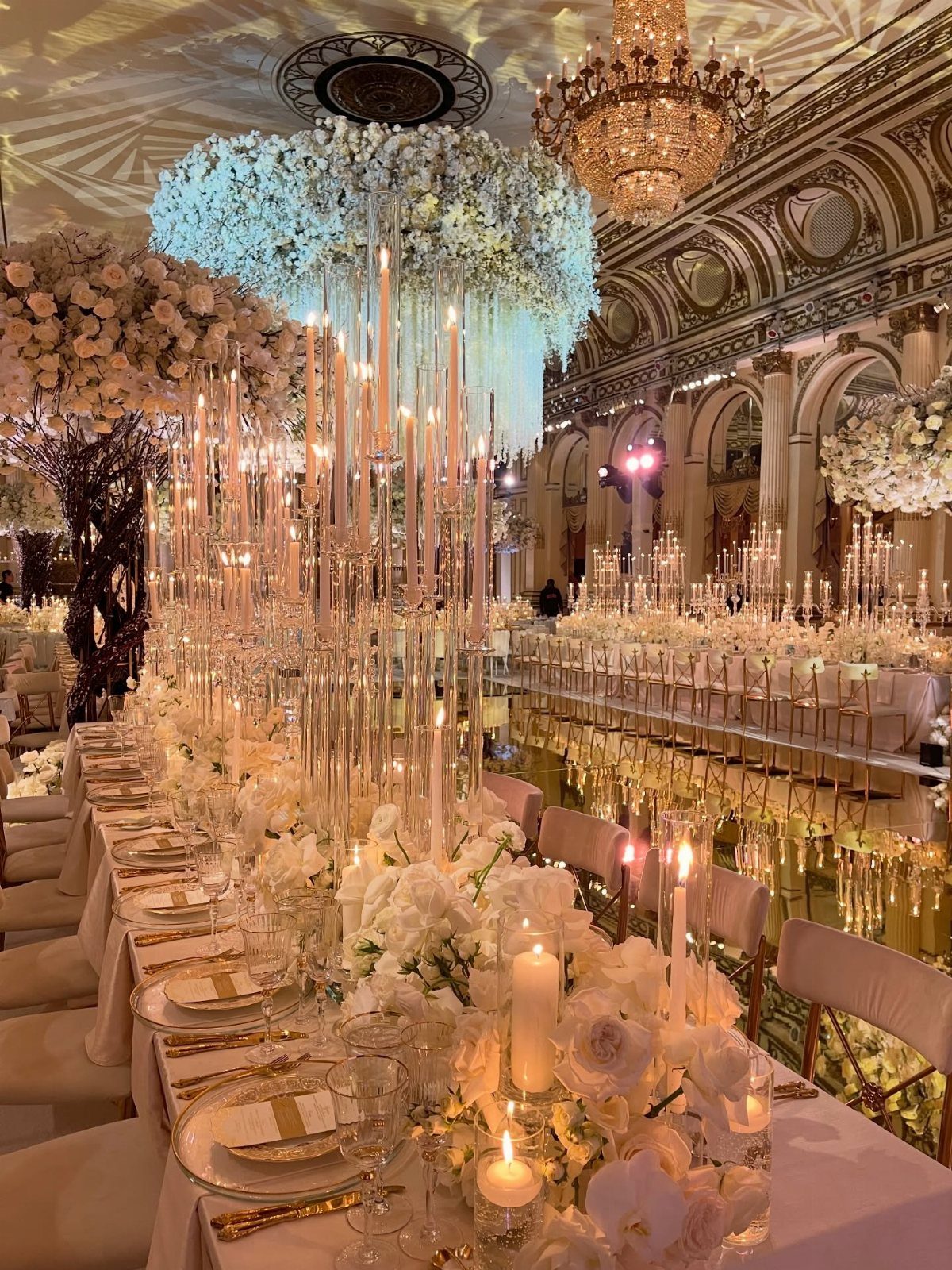 Opulent wedding banquet table with white flowers, gold accents, and crystal chandeliers.