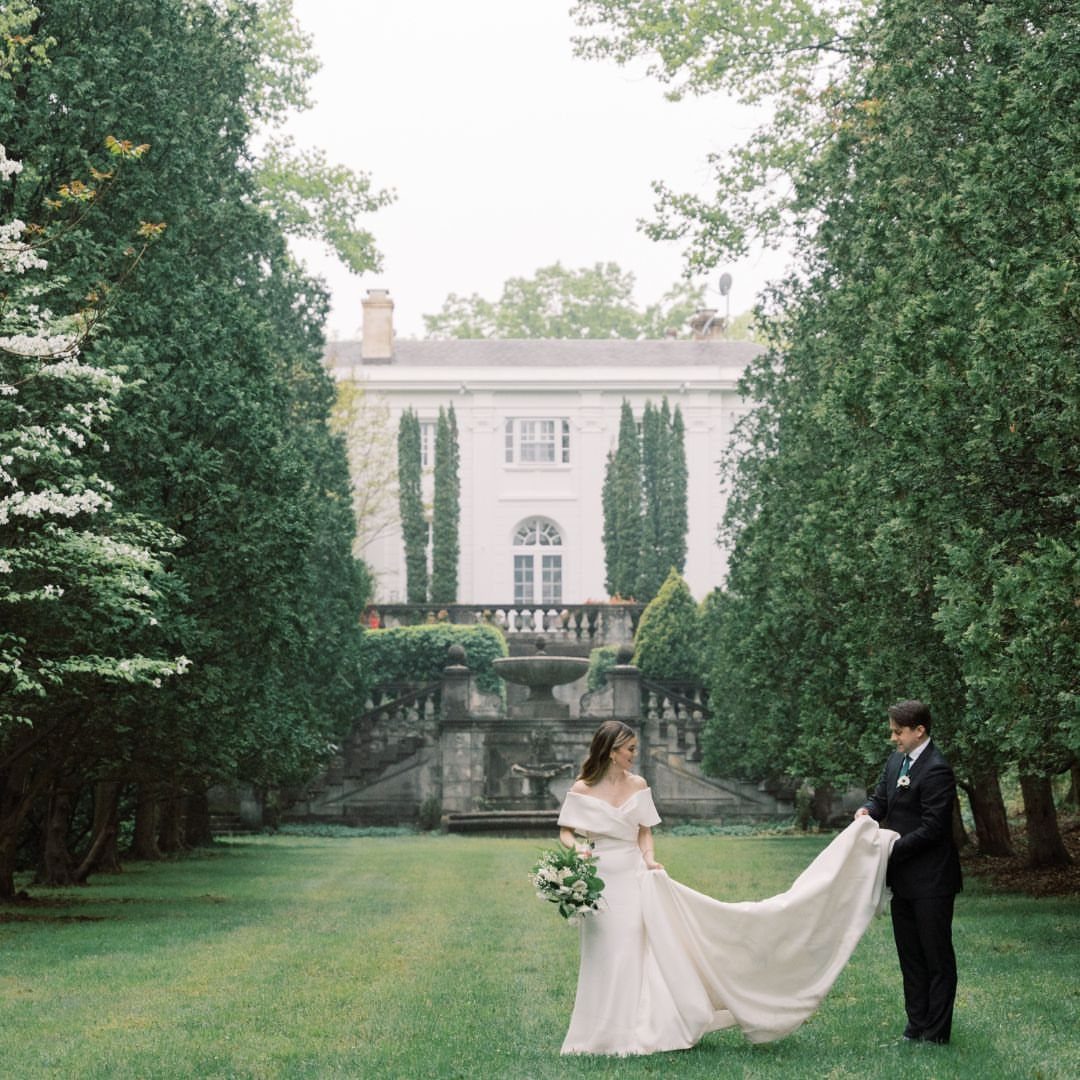 Bride and groom on a green lawn in front of a white mansion