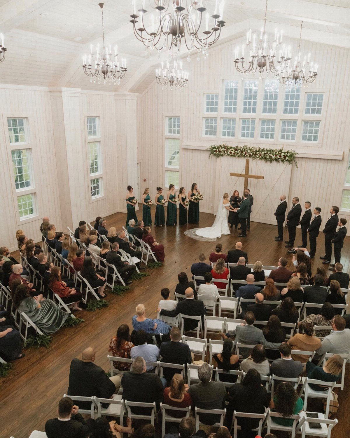 Wedding ceremony in a white chapel with a wooden cross and seated guests.