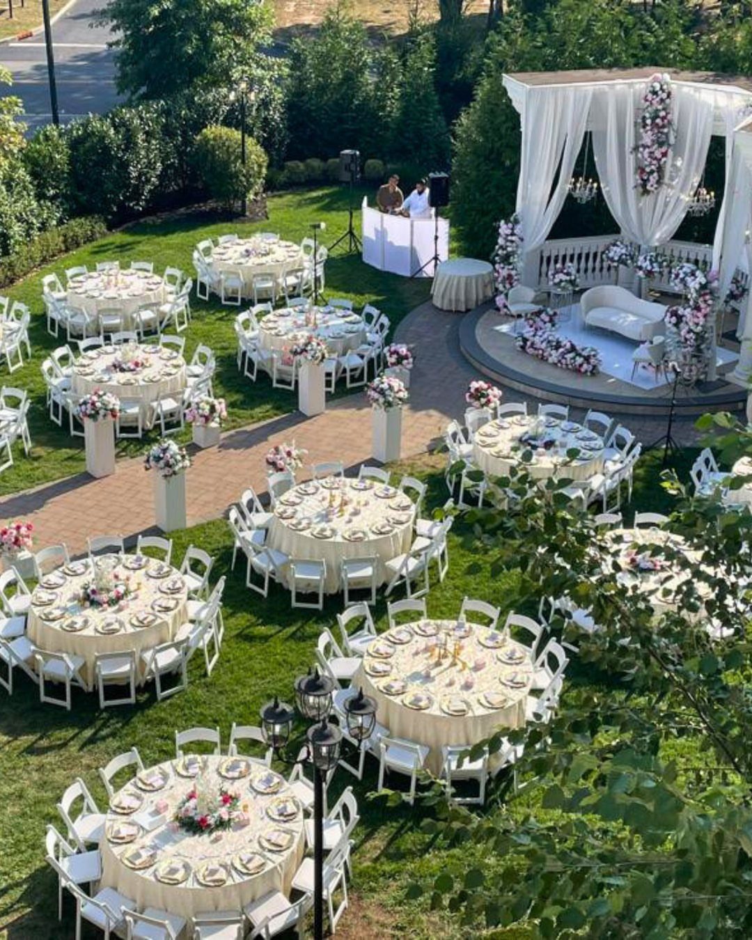 Outdoor wedding reception with white round tables and a draped gazebo on grass