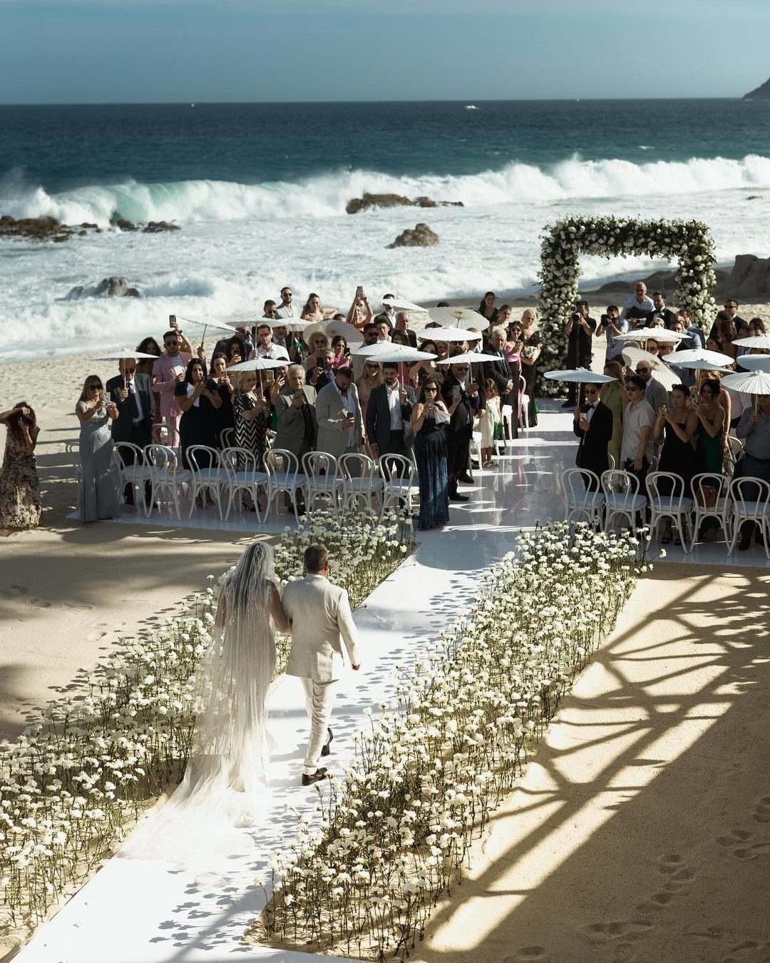 Bride and groom walking down a flower-lined aisle on a beach wedding venue.