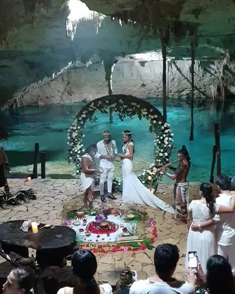 Wedding couple standing under a floral arch inside a turquoise water cenote cave