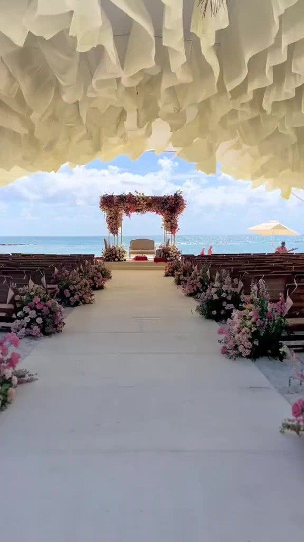 Beach wedding ceremony setup with a floral arch and white aisle under fabric canopy