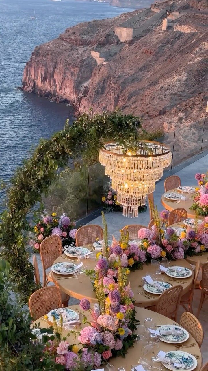 Outdoor wedding reception tables with floral centerpieces overlooking a rocky coastal cliffside