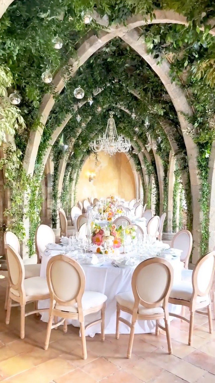 Elegant wedding reception tables under vine-covered stone arches with a crystal chandelier.
