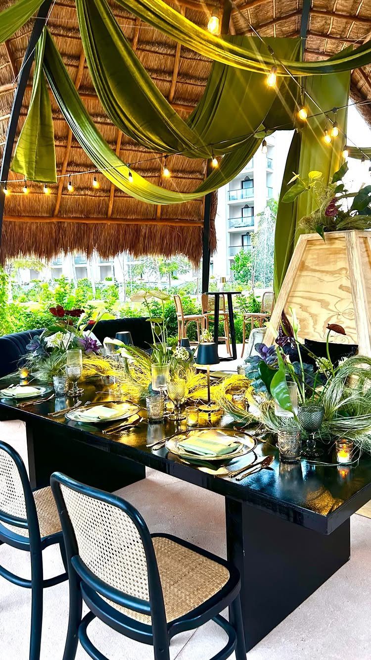 Tropical outdoor dining table with green fabric draping and lush floral centerpieces