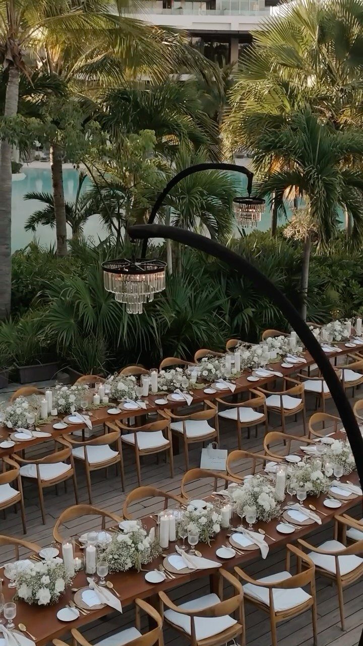 Elegant outdoor wedding reception tables with white flowers and palm trees in Mexico.