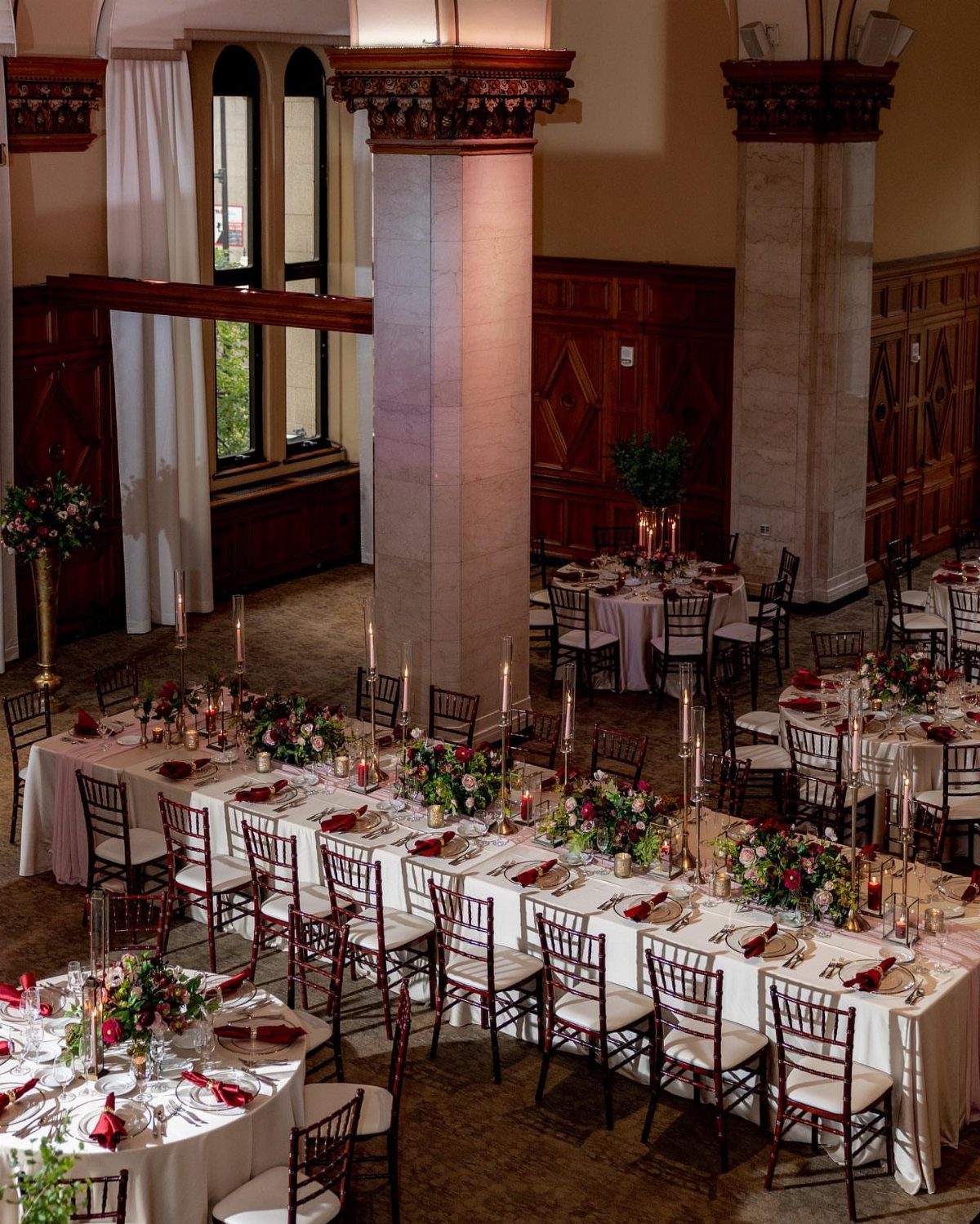 Elegant ballroom setup with long banquet tables, floral arrangements, and stone pillars.
