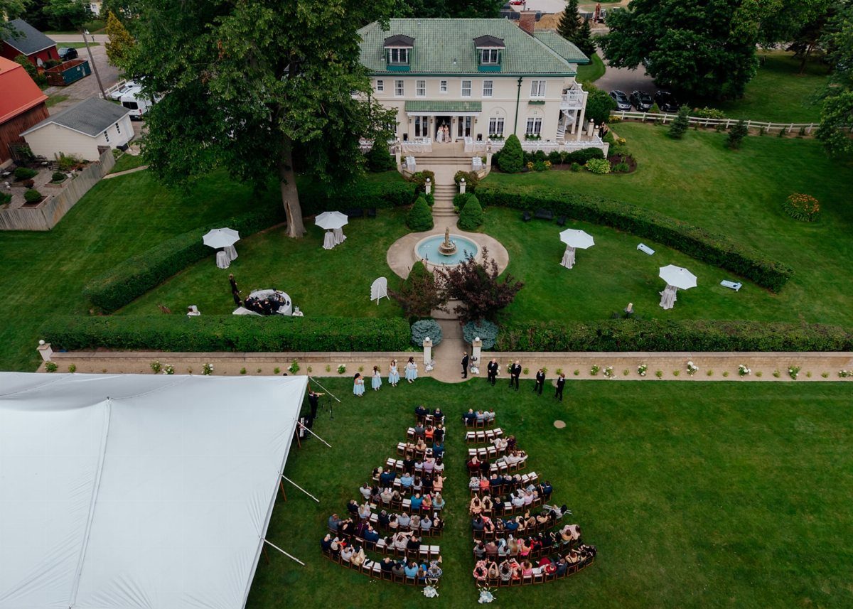 Outdoor wedding ceremony on a lawn with a historic white manor house background.