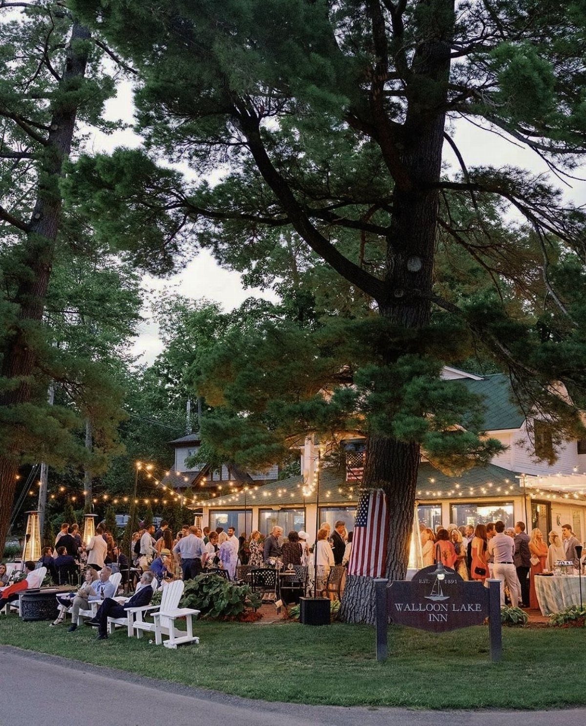 Guests gathering outdoors at Walloon Lake Inn under string lights and large pine trees.