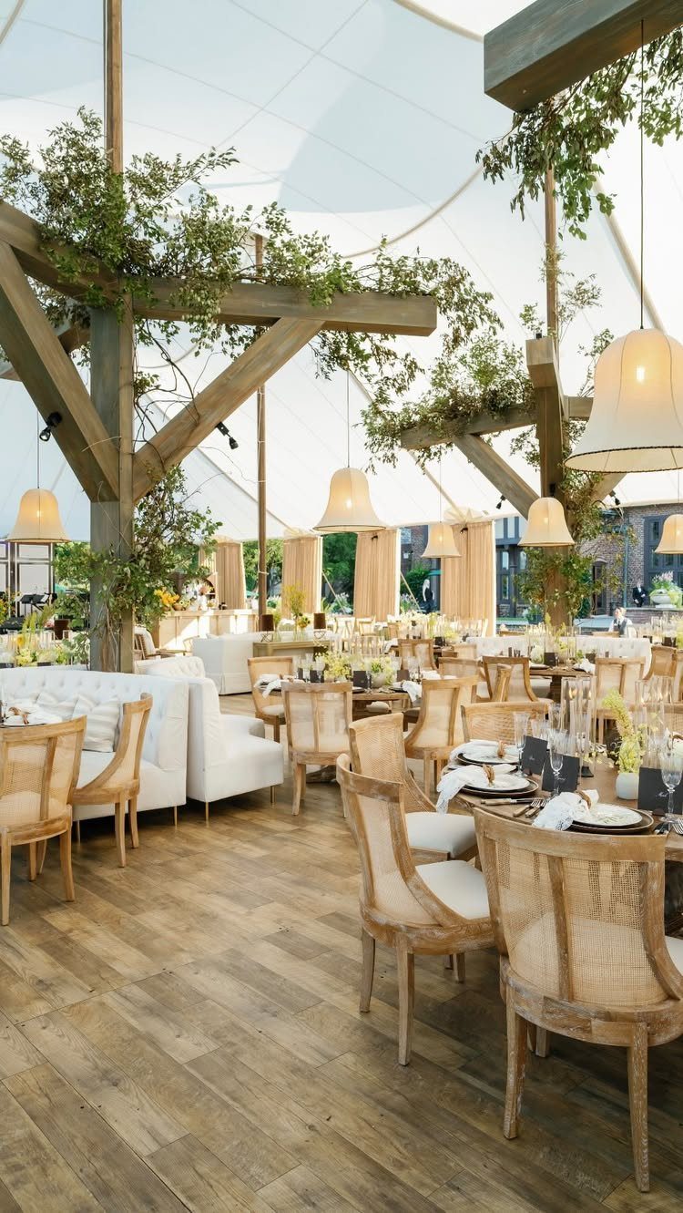 Elegant wedding reception setup under a white tent with wooden beams and greenery.