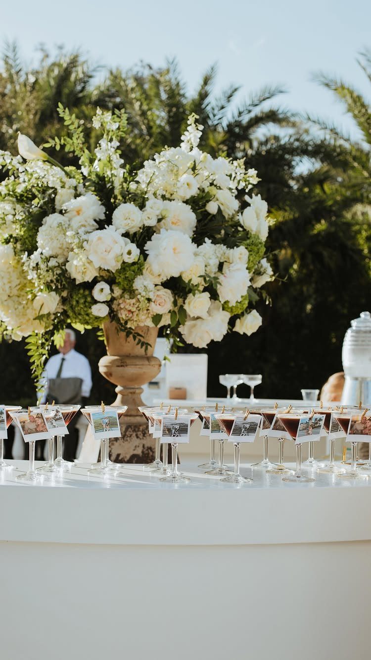 White floral centerpiece and drink glasses with photo cards on a white table.