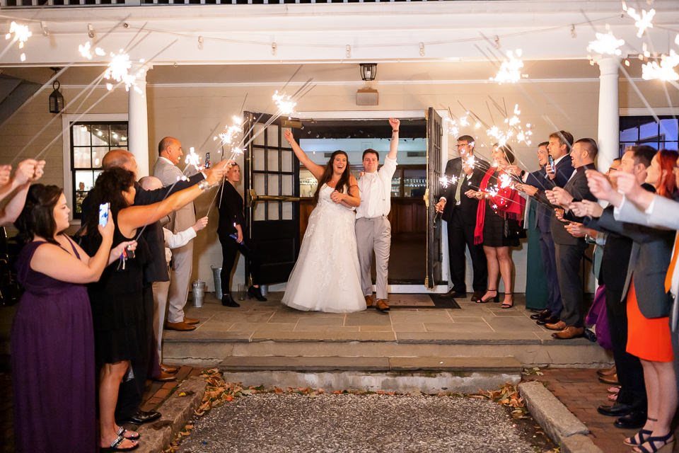 Bride and groom cheering while guests hold sparklers during a wedding send-off.