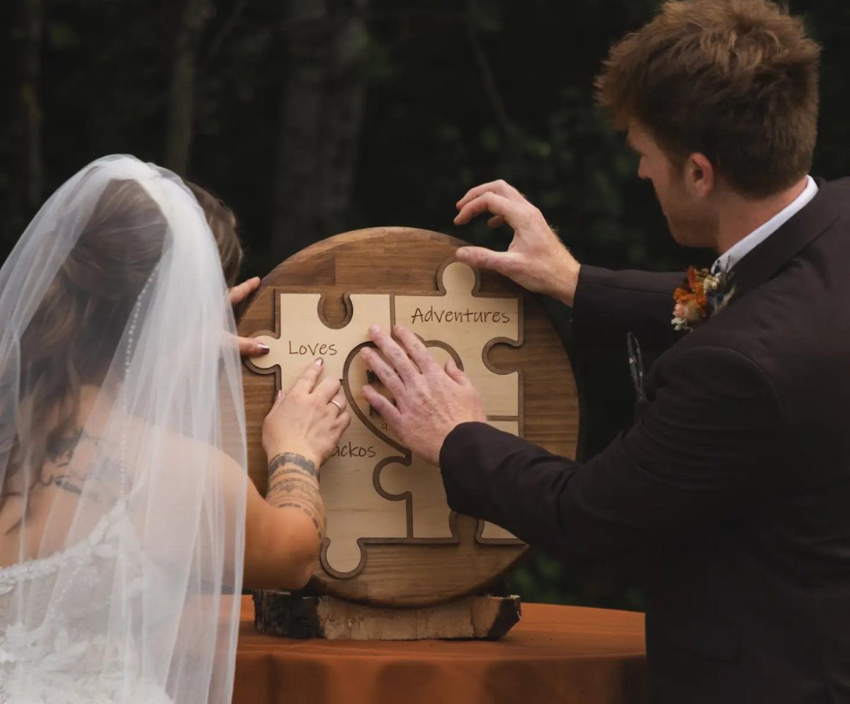 Bride and groom assembling a large wooden puzzle during their wedding ceremony outdoors.