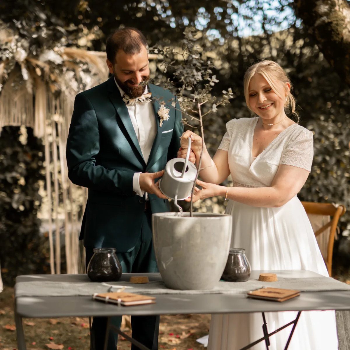 Bride and groom watering a small tree in a pot during their wedding ceremony