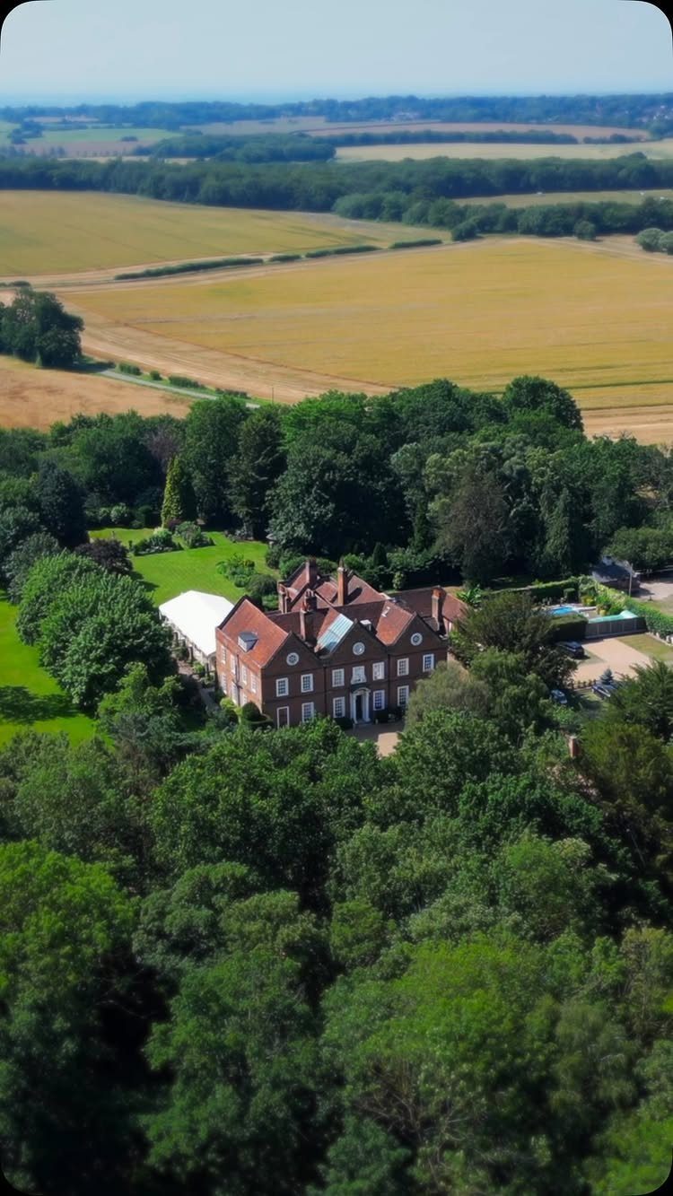 Red brick manor house with a white marquee tent surrounded by green forests