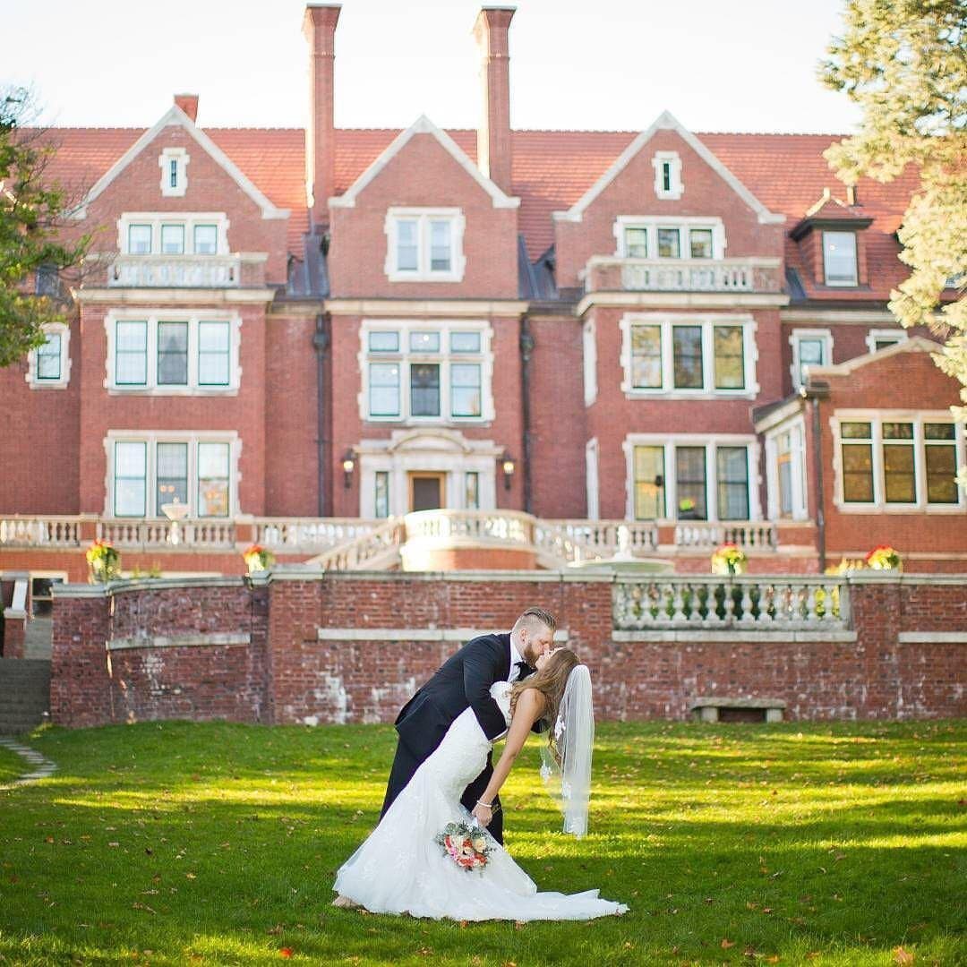 Bride and groom kissing on a lawn in front of a red brick mansion
