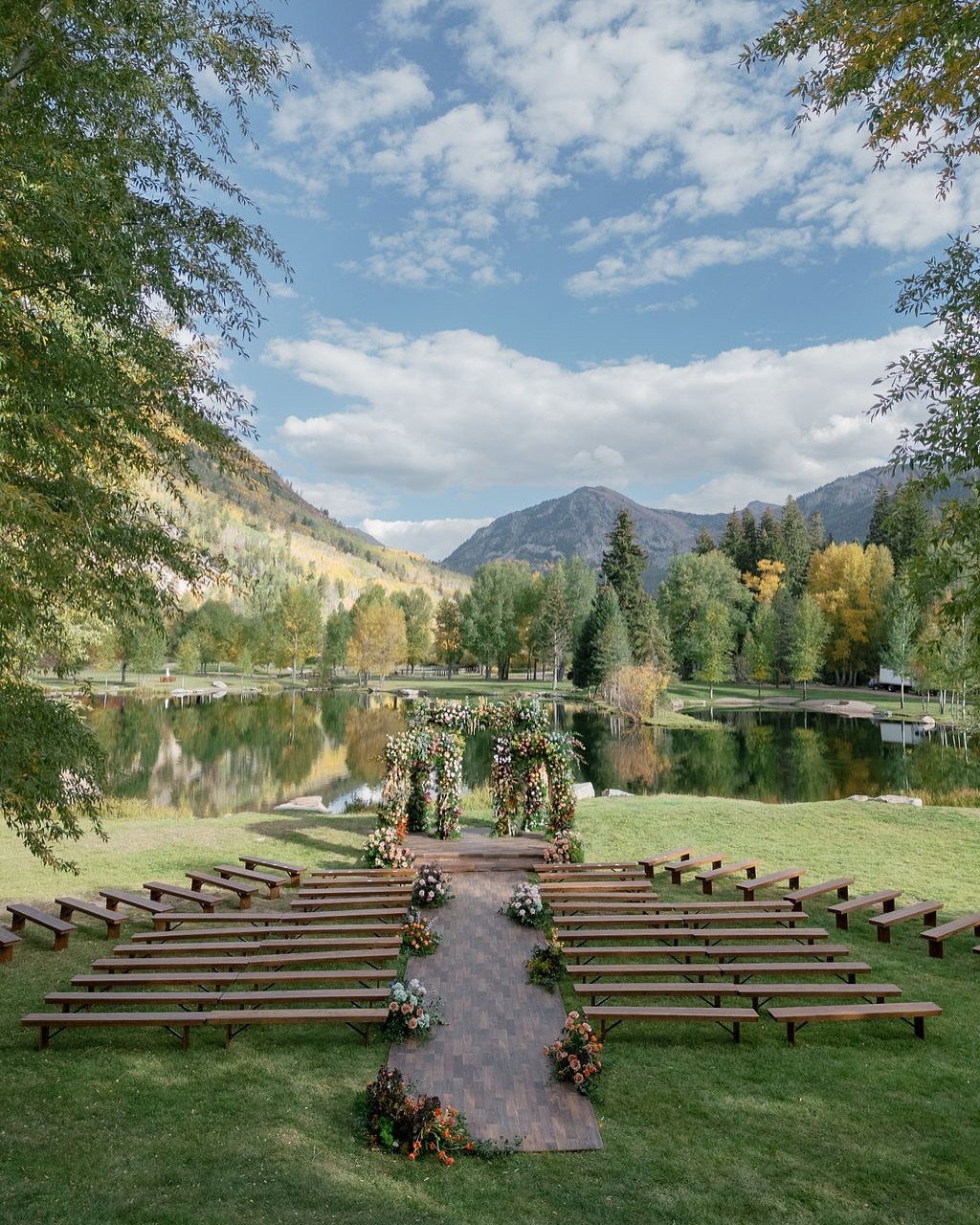 Outdoor wedding ceremony setup with wooden benches and floral arch by a mountain lake