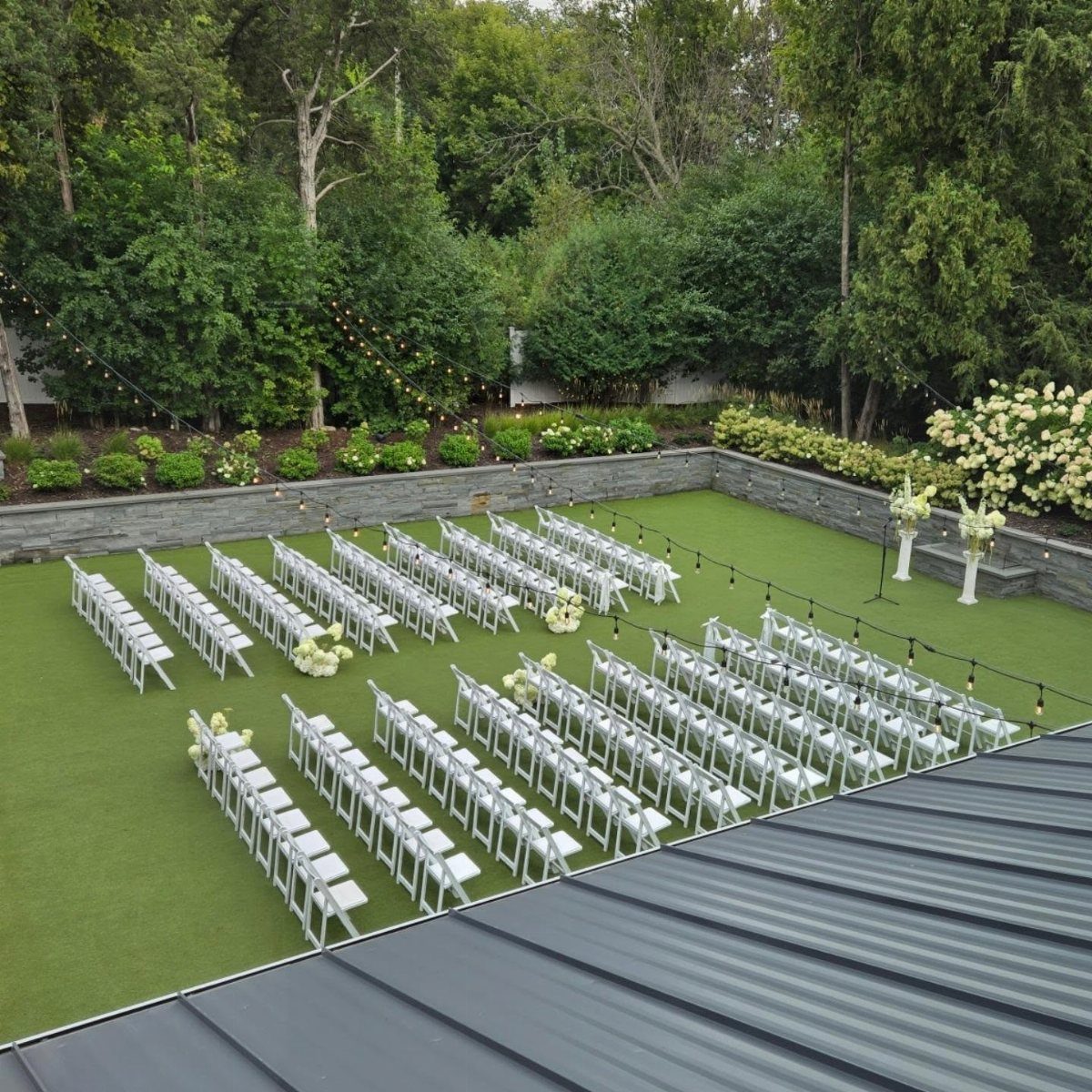 White folding chairs arranged on green turf for an outdoor wedding ceremony.