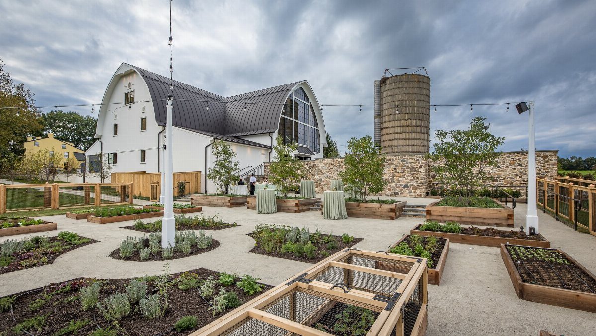 Modern white event building with curved roof next to a concrete silo and garden