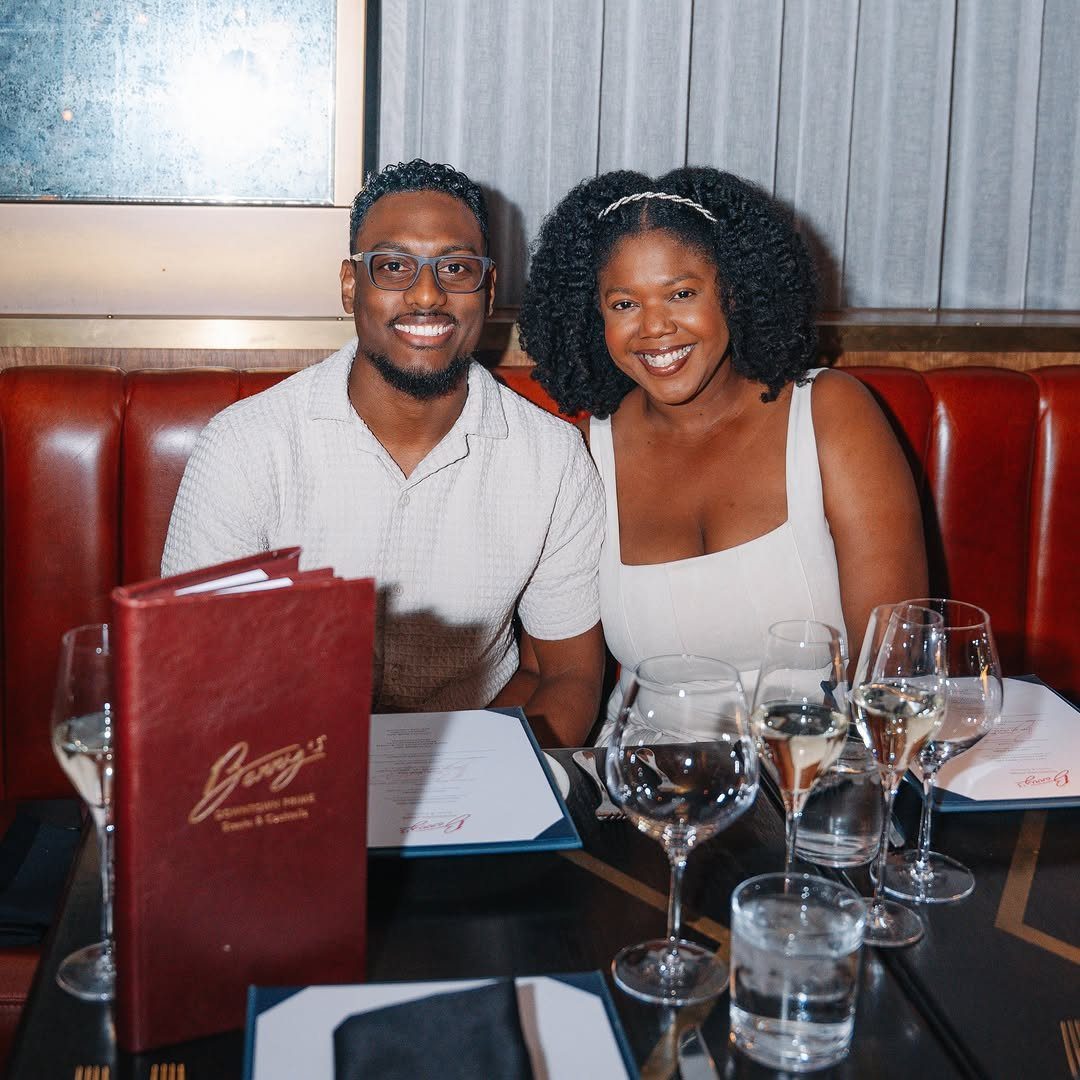 Smiling couple sitting in a red leather restaurant booth with wine glasses and menus.