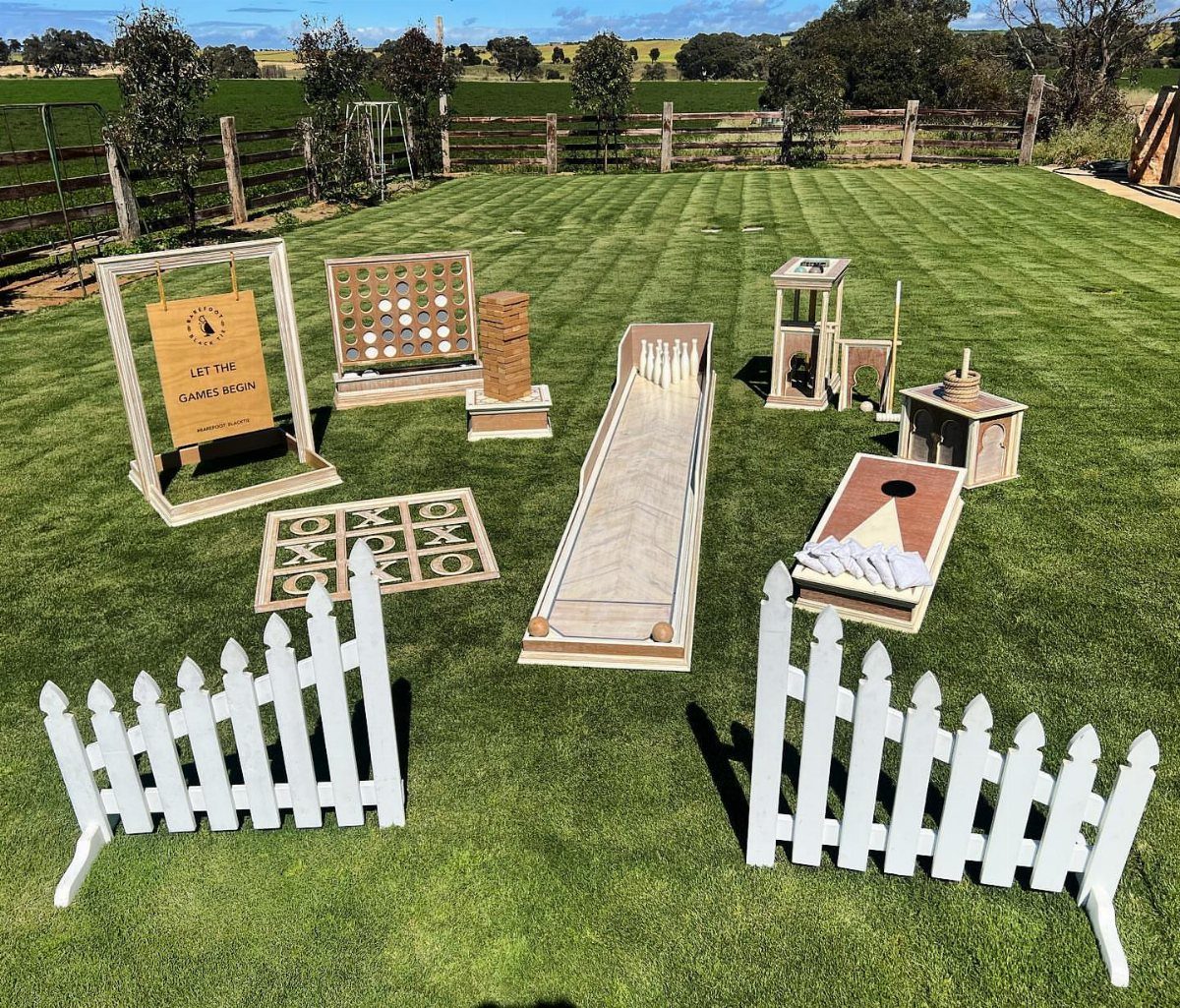 Wooden lawn games arranged on a green grass field with white picket fences.