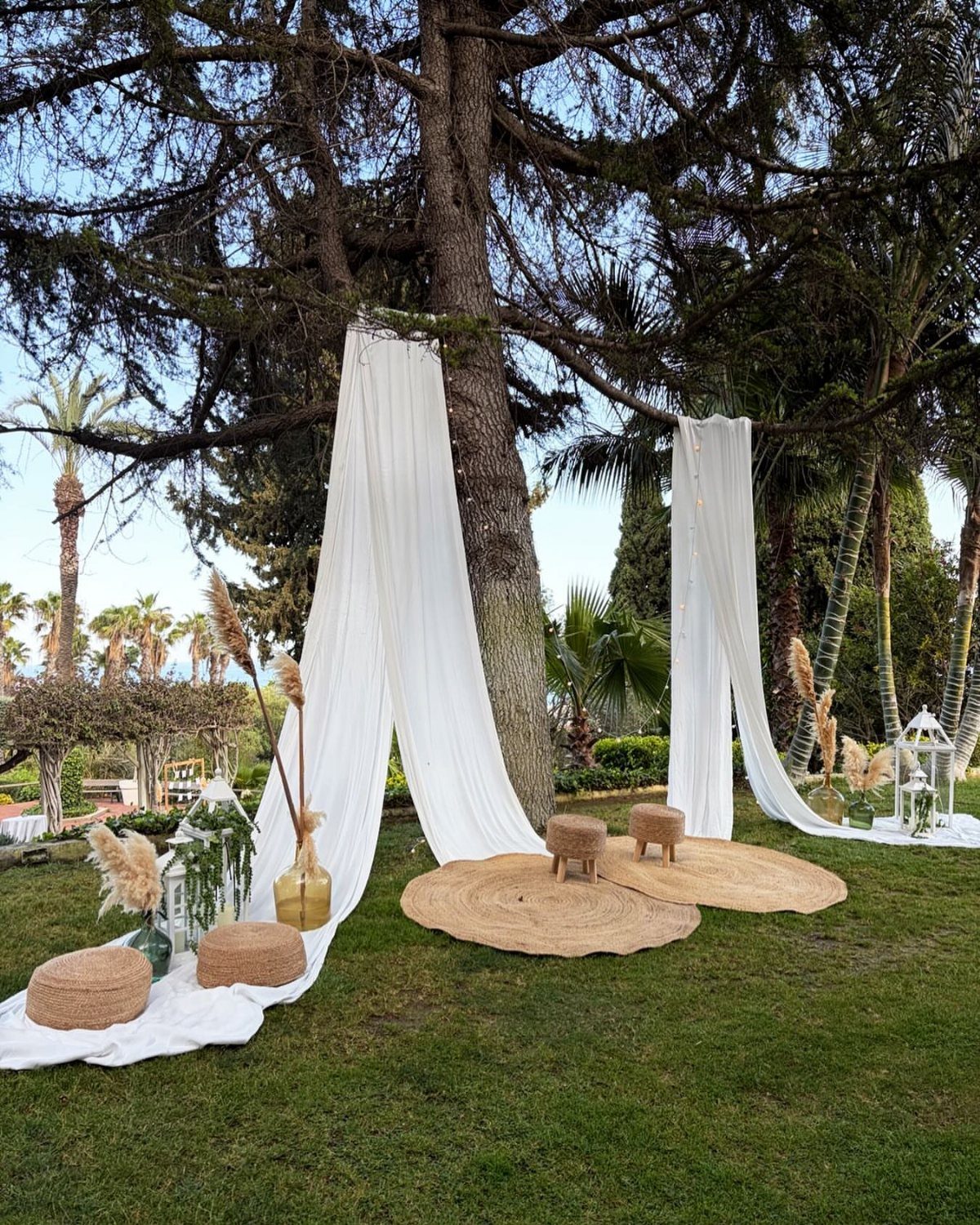 Boho lounge area with white drapes, layered jute rugs, and woven stools outdoors.