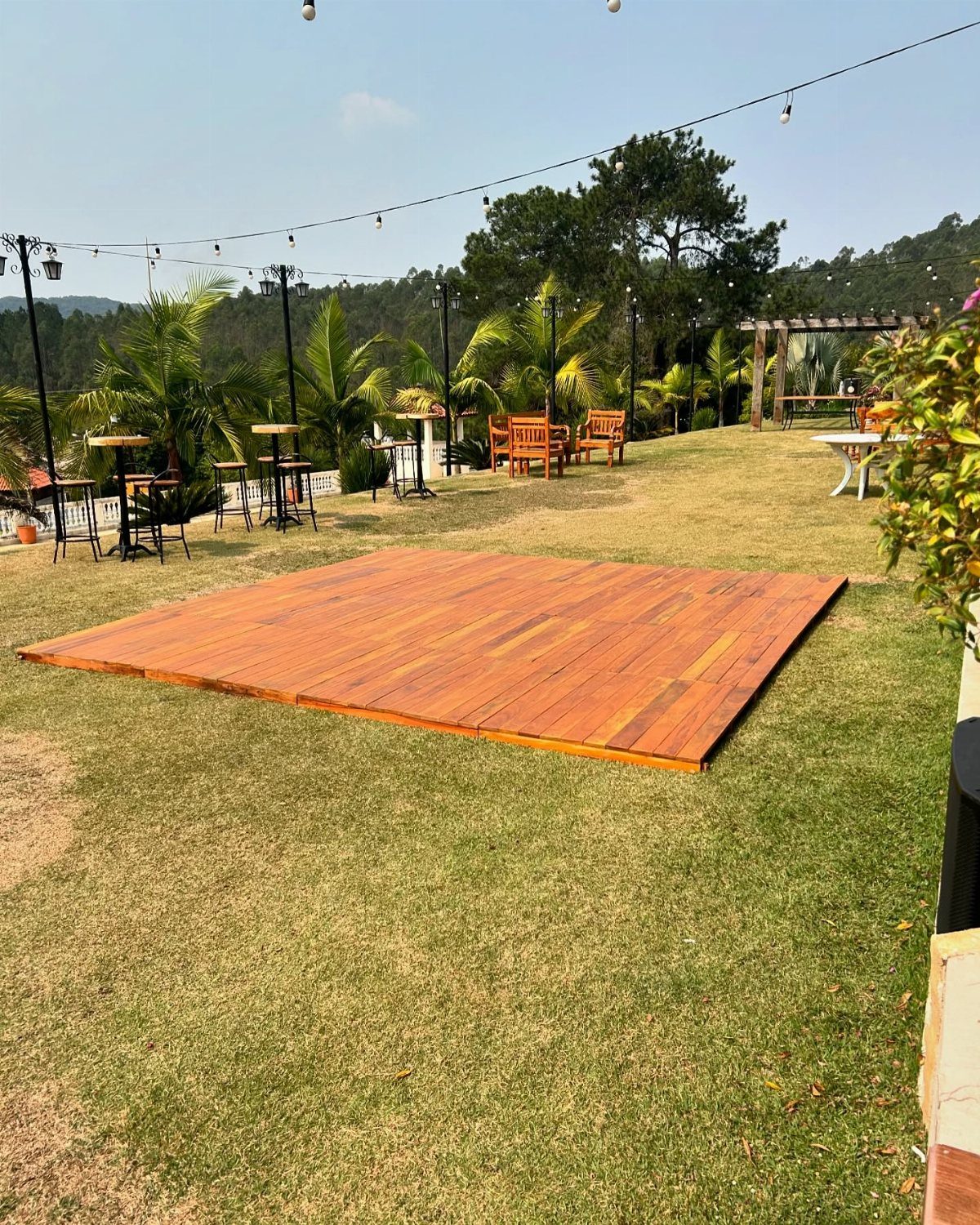Wooden dance floor platform on a grassy lawn with outdoor wedding furniture and lights.