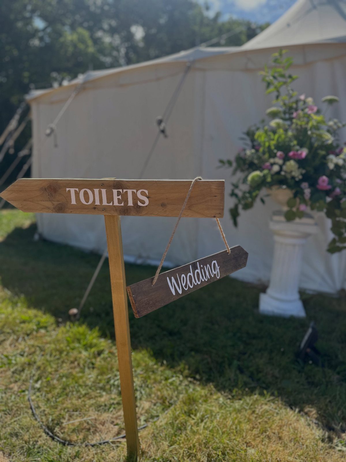 Wooden directional signpost with Toilets and Wedding signs in front of a white tent