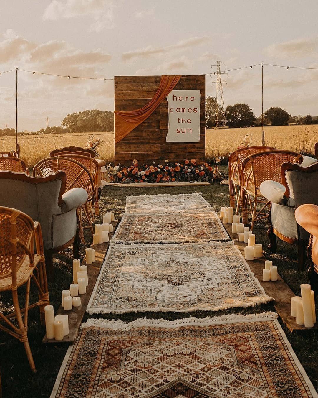 Patterned rug aisle with white pillar candles leading to a wooden ceremony backdrop.