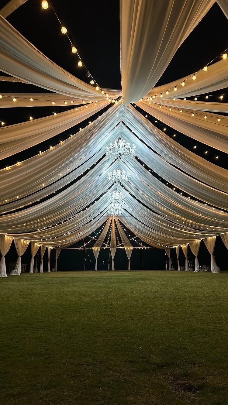 White draped event tent with crystal chandeliers and string lights over green grass