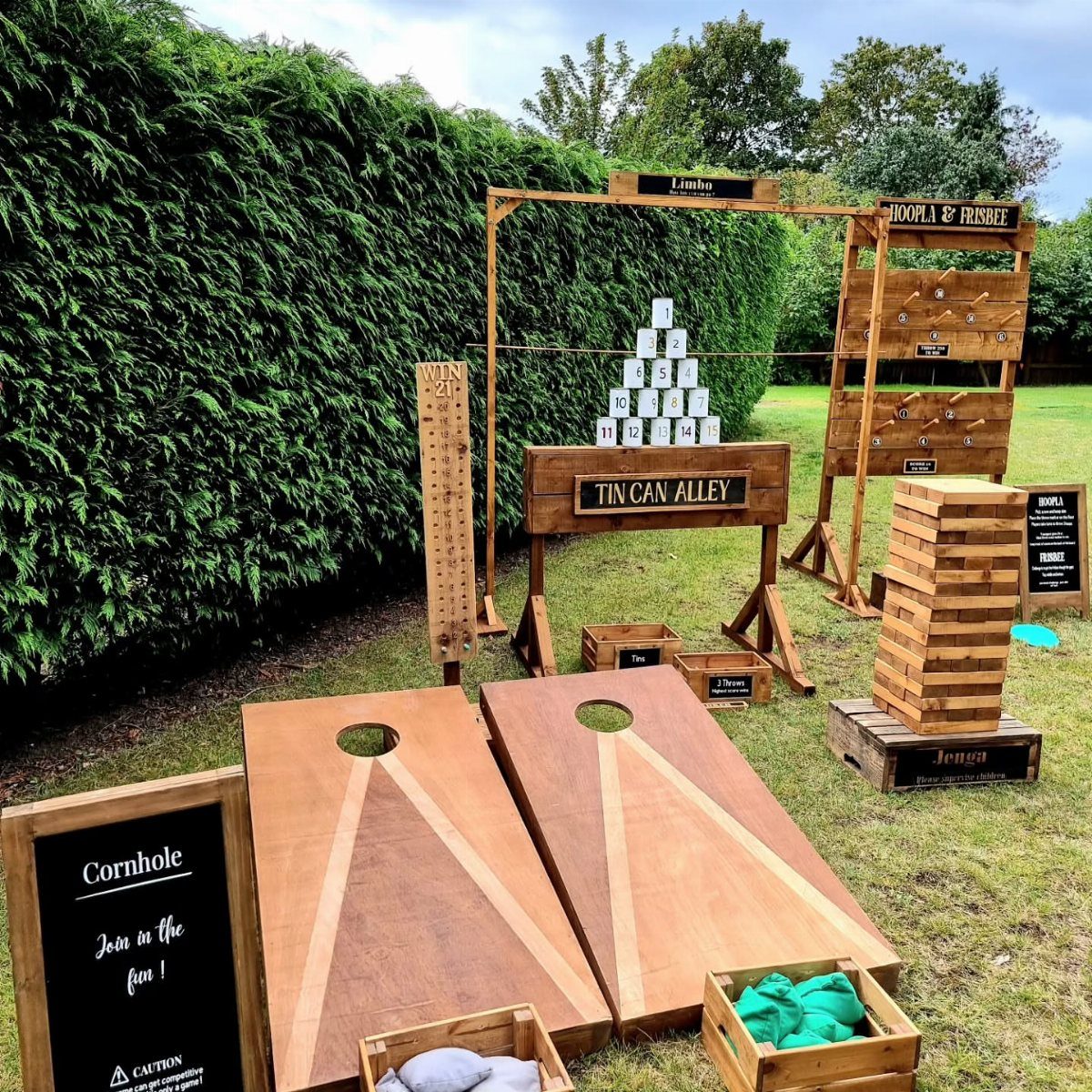 Wooden outdoor games including cornhole and giant Jenga set up on a lawn.