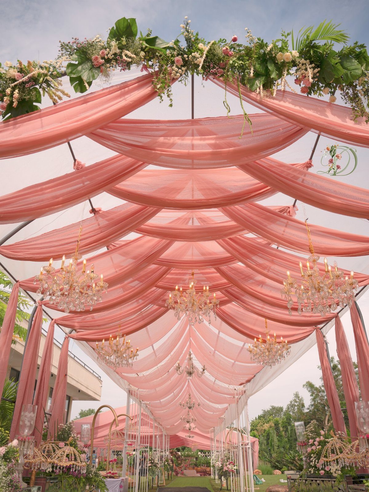 Peach fabric drapes and crystal chandeliers decorating an outdoor wedding venue ceiling.