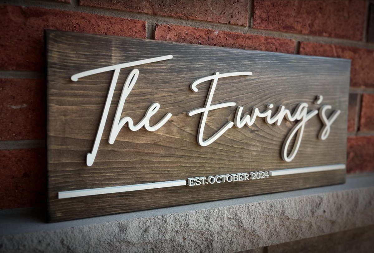 Personalized wooden sign with white cursive text resting on a stone ledge.
