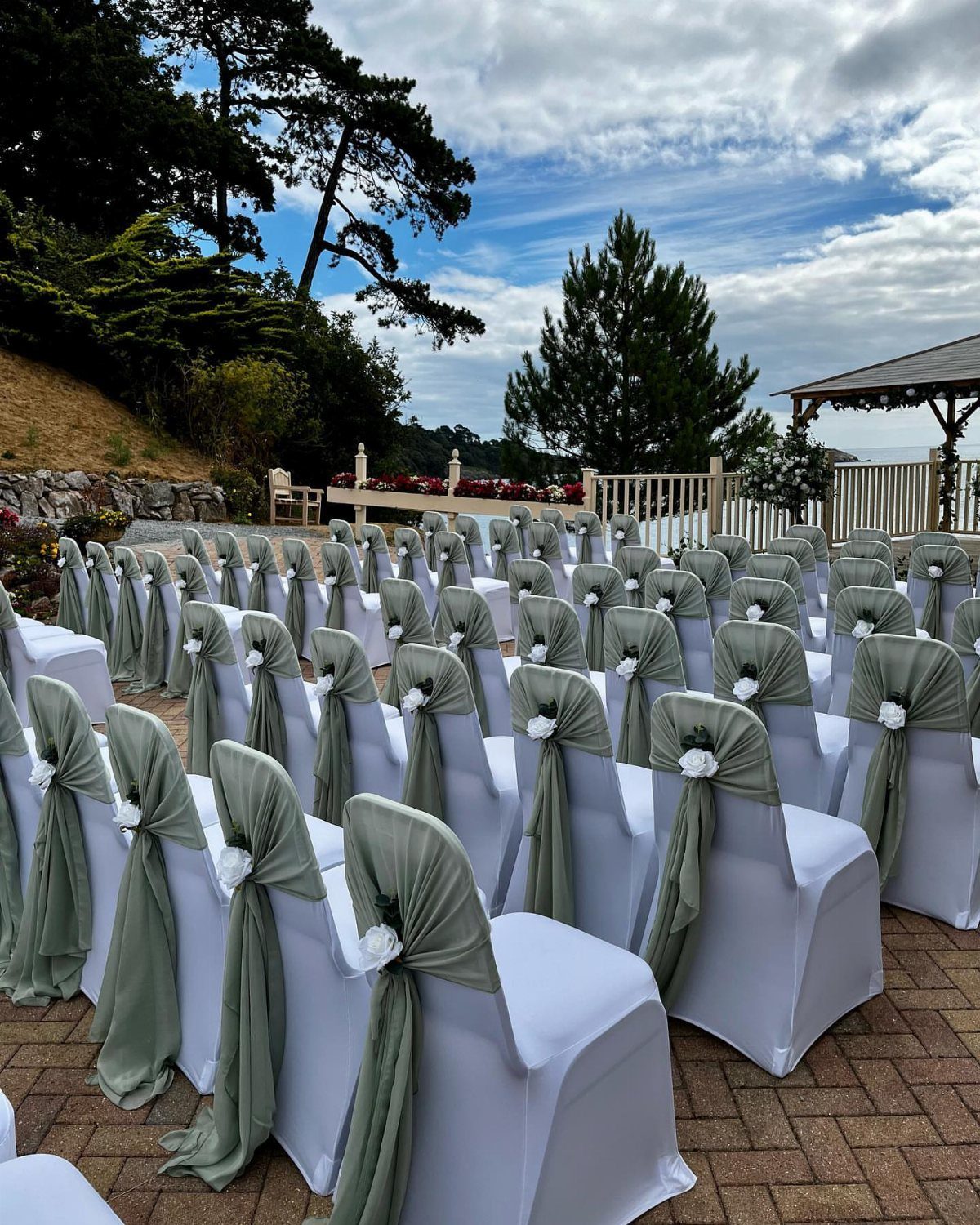 White wedding chairs with sage green fabric sashes and small white floral accents.