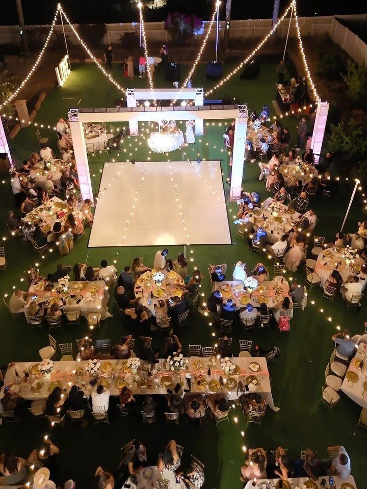 Outdoor wedding reception at night with overhead string lights and a white dance floor.