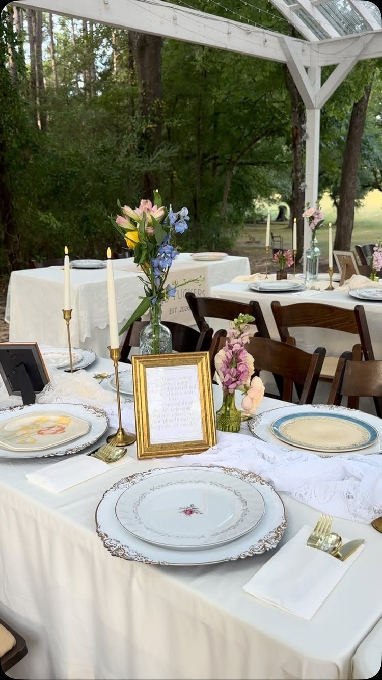 Wedding table setting with white floral plates, gold candle holders, and colorful flowers.