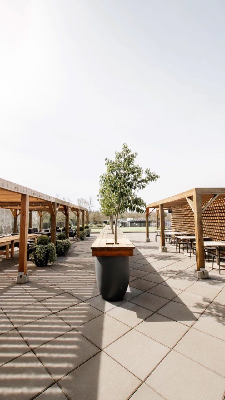 Modern outdoor patio with wooden pergolas, stone pavers, and a central planter tree.