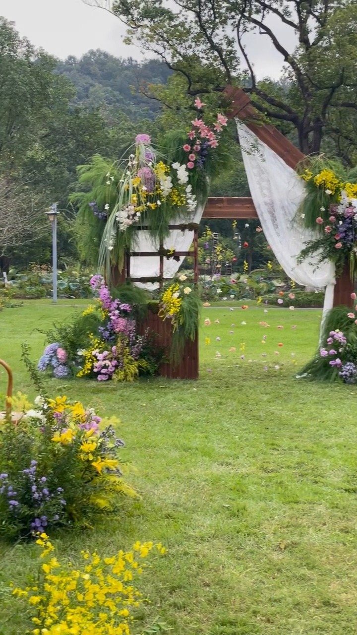 Wooden wedding arch with colorful flowers on a green lawn with distant hills.