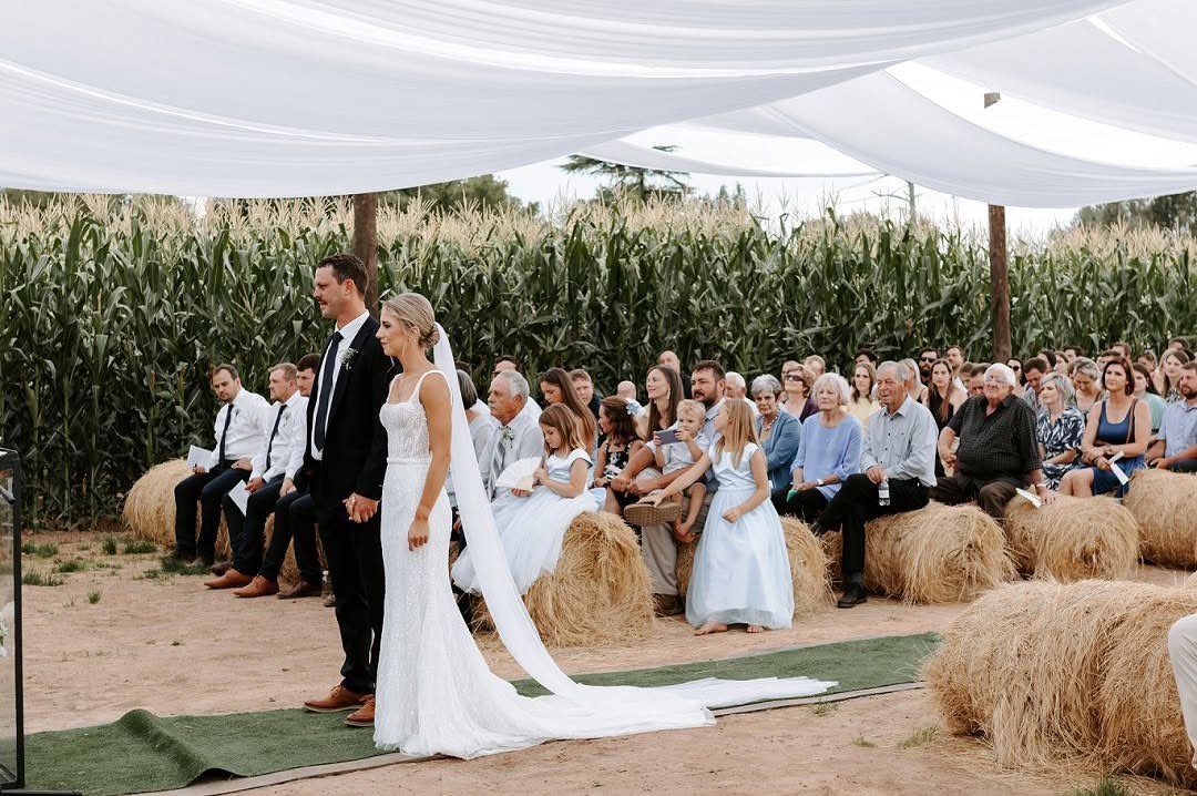 Bride and groom standing at an outdoor wedding ceremony with hay bale seating.