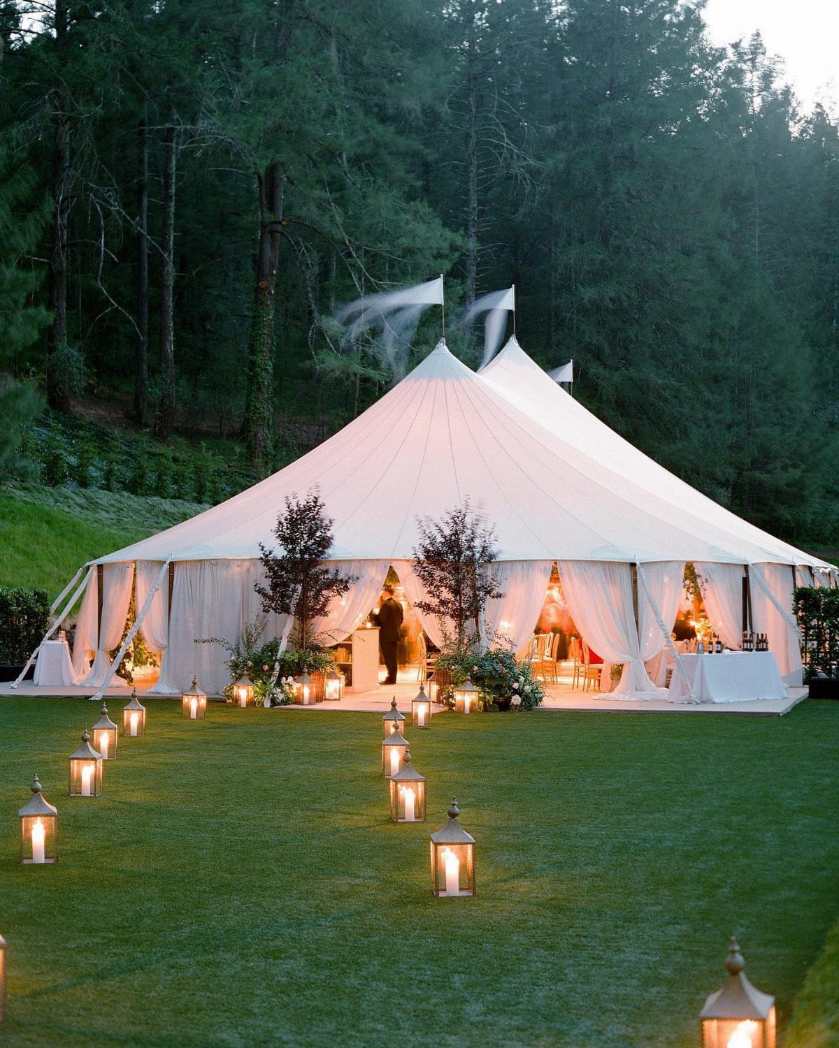 Large white event tent on a grassy lawn with lanterns at dusk.