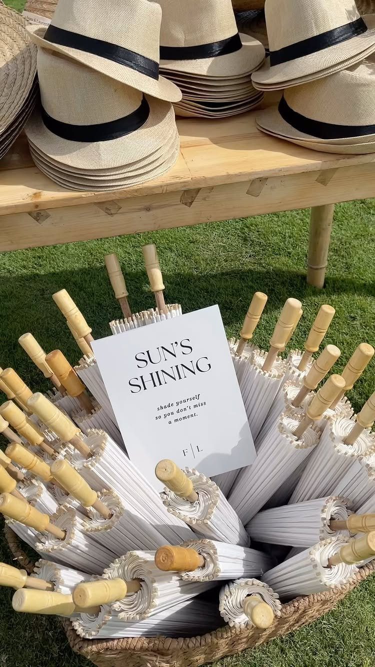 Beige straw hats and white parasols with a sign on a grassy lawn.
