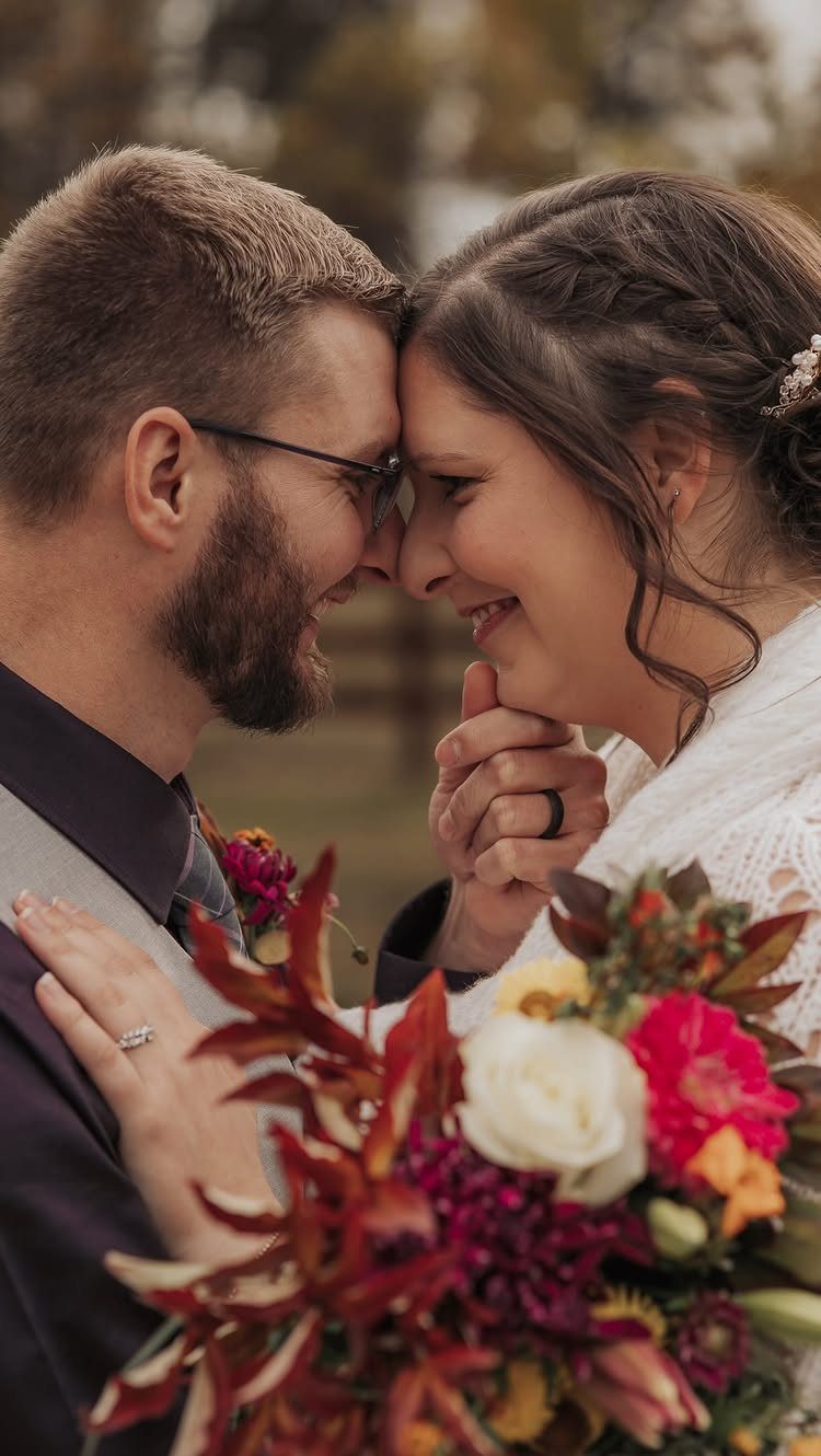 Bride and groom touching foreheads and smiling with a colorful autumn bouquet.