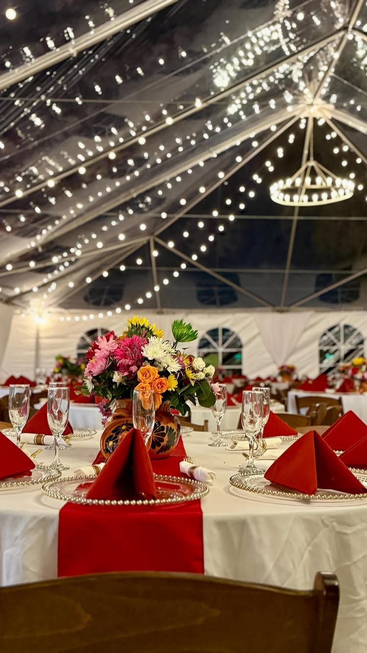 Wedding reception tables with red napkins under a clear tent with fairy lights.
