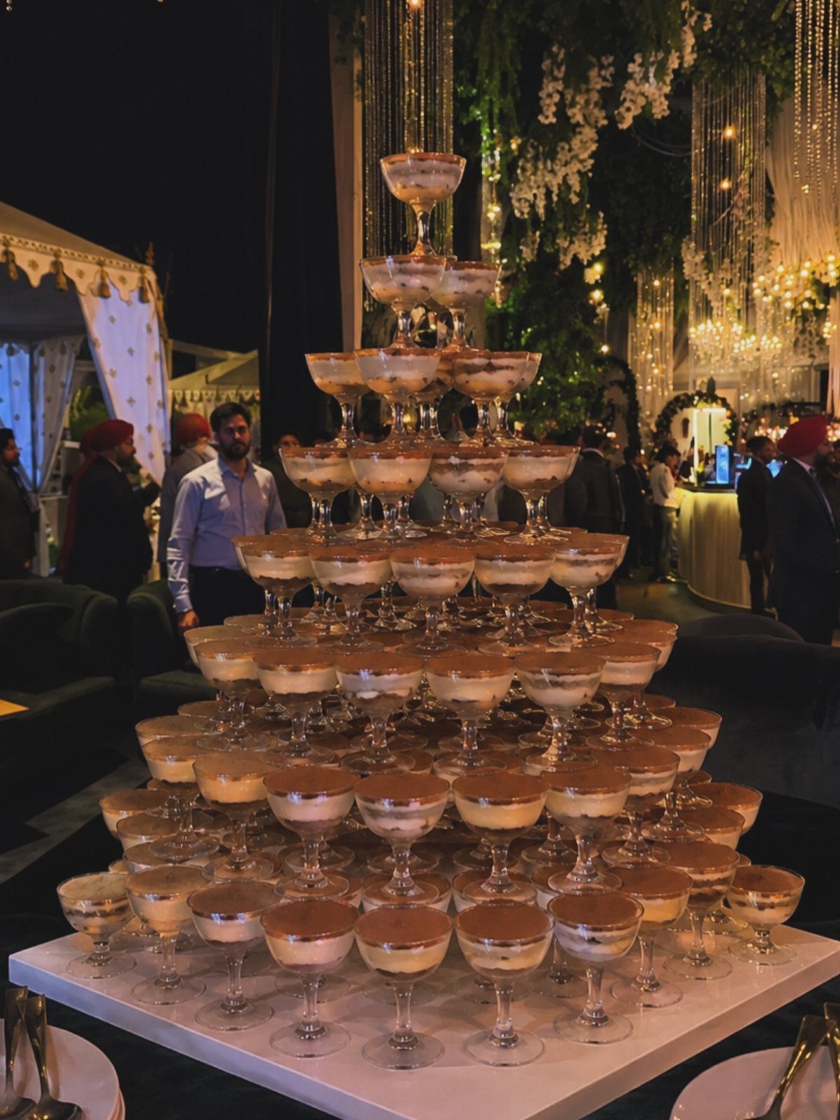 Pyramid of layered dessert cups on a white table at an outdoor wedding reception.