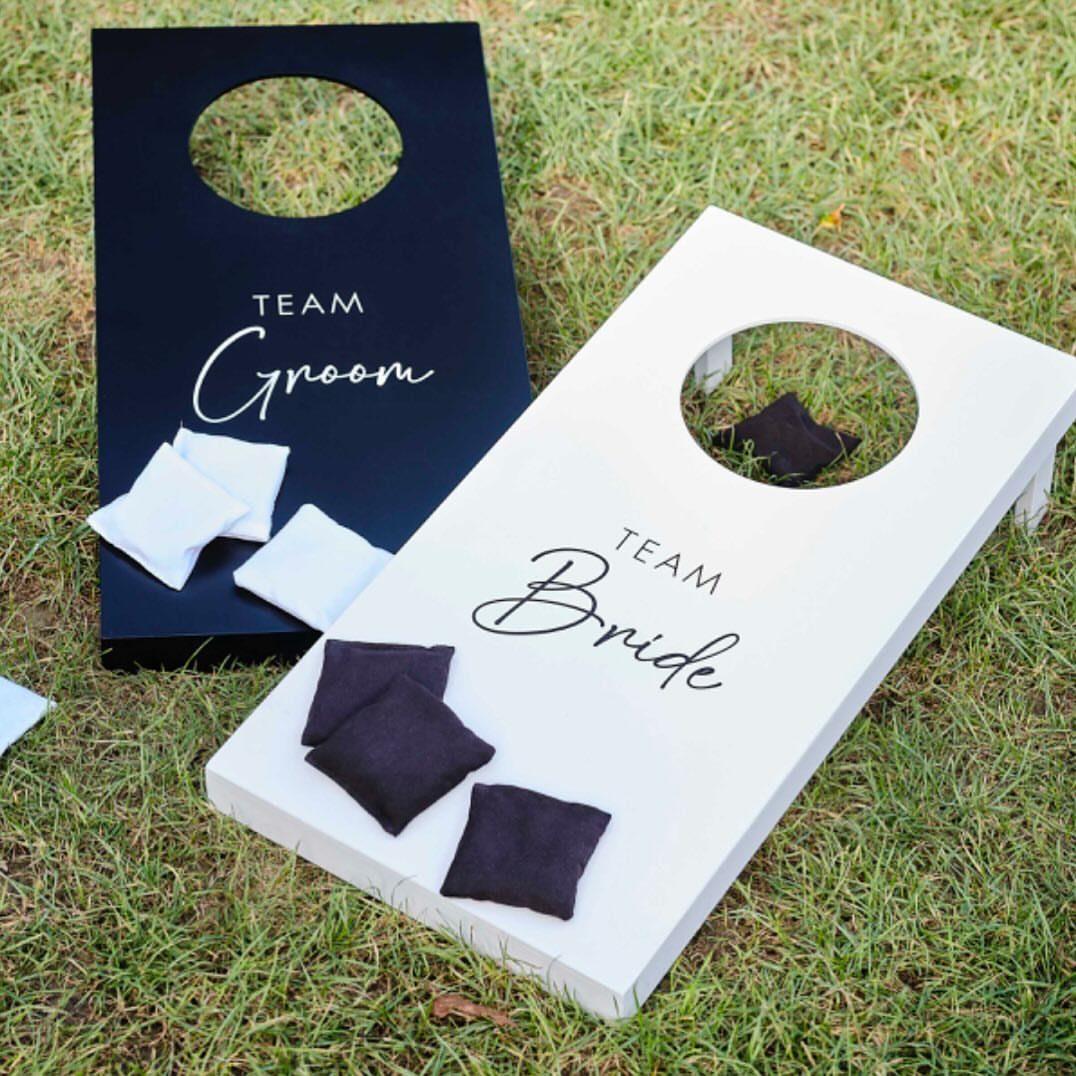 Cornhole boards labeled Team Groom and Team Bride on a green lawn.