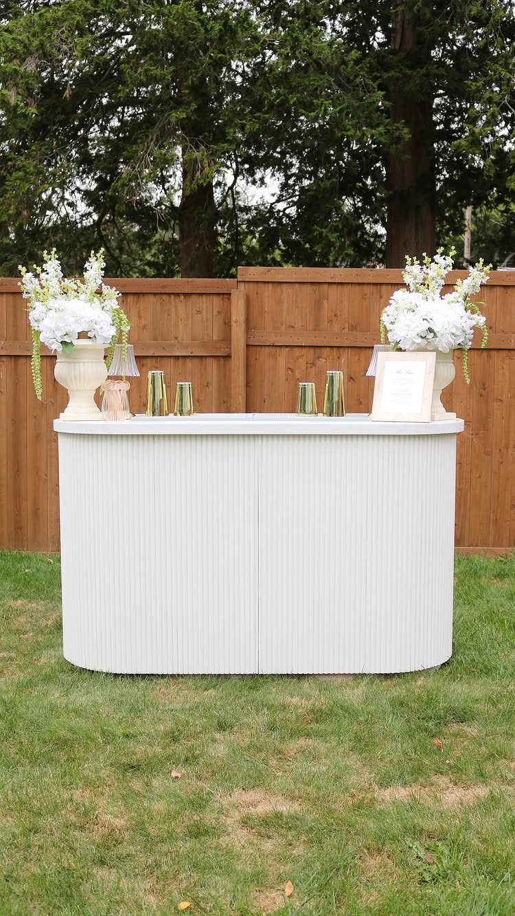 White ribbed bar counter with white flowers on a lawn by a fence